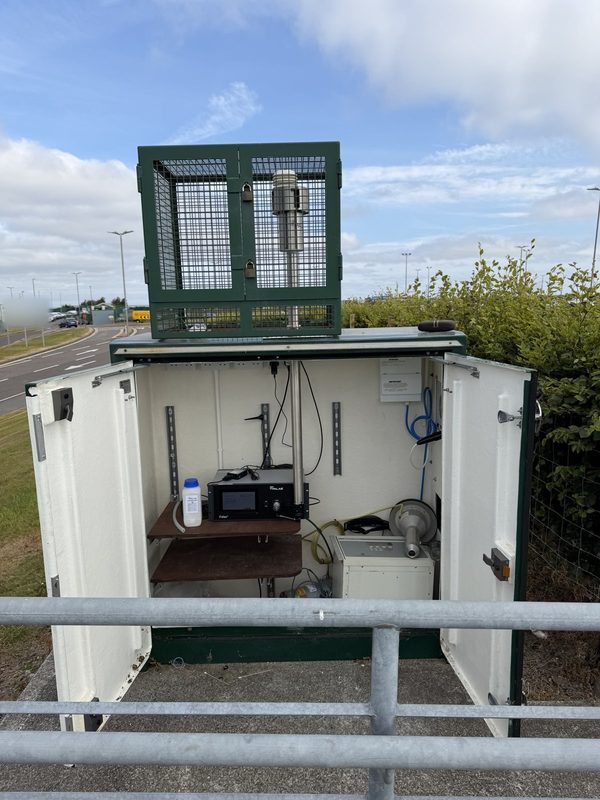 Ambient air quality monitoring station with a particulate monitor inside and a caged inlet on the roof
