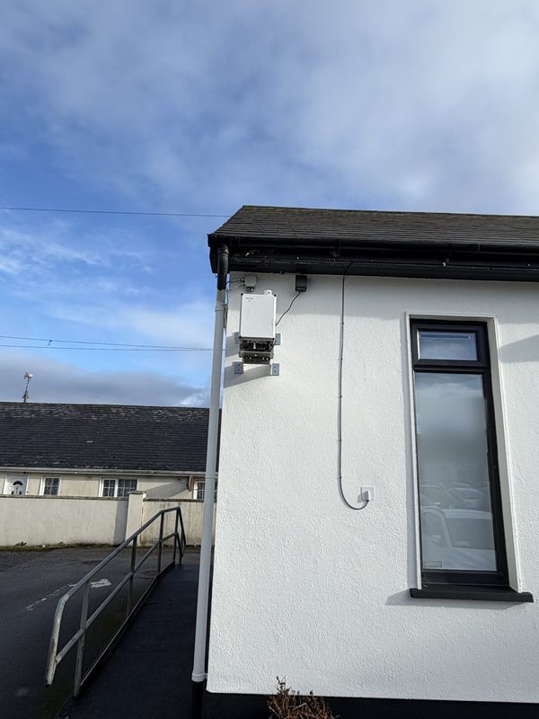 Compact particulate monitor mounted high on the wall of a white building