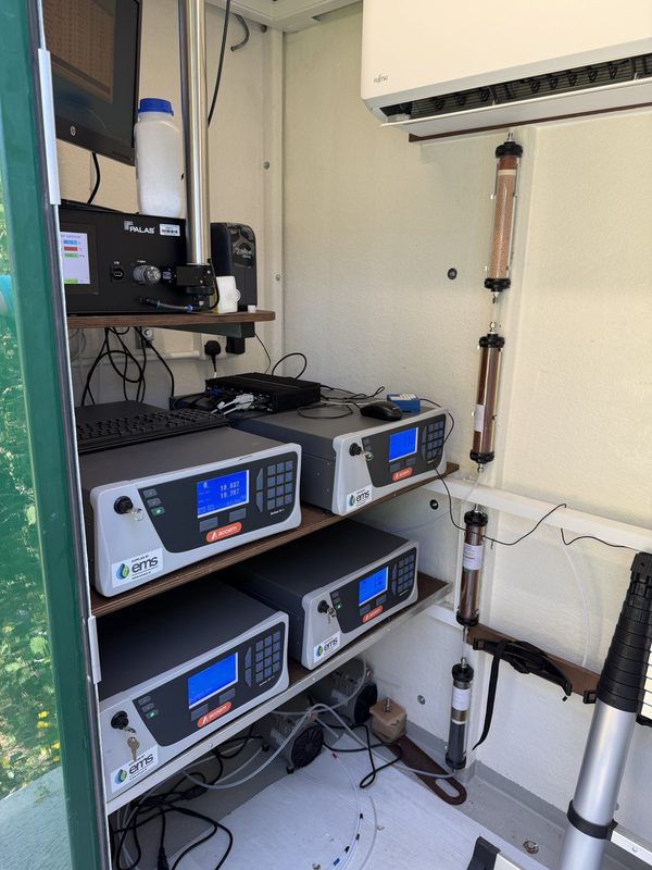 Rack of ACOEM gas analysers with EMS labels inside an air monitoring station